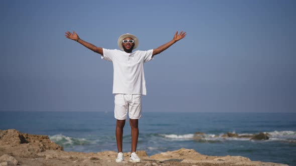 Wide Shot of Smiling African American Tourist Stretching Hands Standing on Cliff with Mediterranean