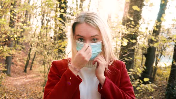 Portrait of a young beautiful woman putting on Corona safety mask amidst orange brown autumn forest