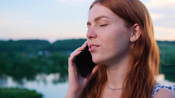 Happy Young Beautiful Redhaired Woman Talking on Mobile Phone Near Lake