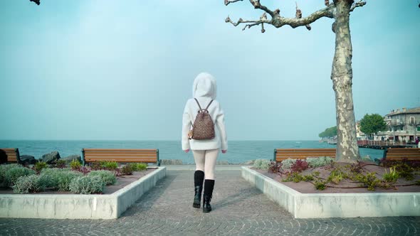 Woman Walks on Embankment Coming Closer to Lake Garda