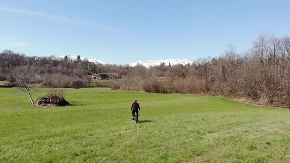 Aerial: man having fun by riding mountain bike in the grass on sunny day, scenic alpine landscape