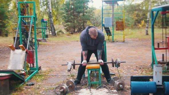 A Tattooed Man Bodybuilder Pumping His Hands with the Dumbbells Made of Bricks and Weights