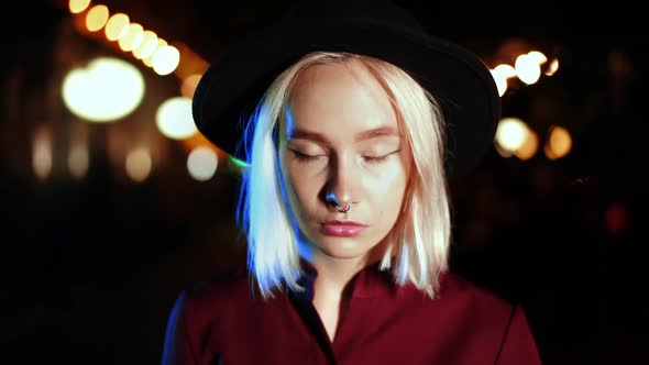 Millennial Hipster Woman with Blond Hairstyle Walking City Street at Night. Hat, Nose Piercing