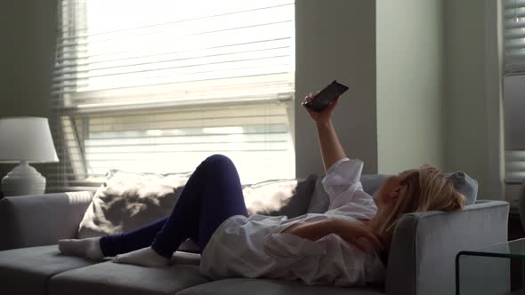 A Relaxed Young Woman Holds a Smartphone Looks at the Screen of a Mobile Phone Enjoys Using Mobile