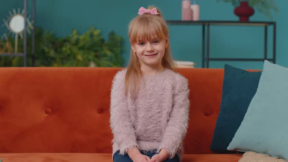 Portrait of Little Adorable Child Girl Sitting Alone on Sofa at Home Looking at Camera and Smiling