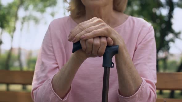 Sad Grandmother Leaning on Walking Stick Sitting on Bench in Park, Nursing Home