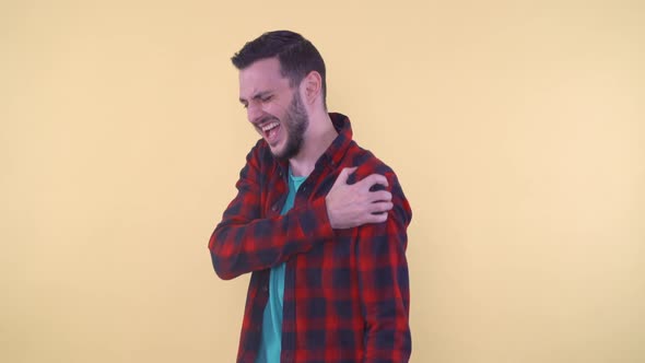 Young Man in Red Shirt Suffering From Shoulder Pain Massaging It with His Right Hand