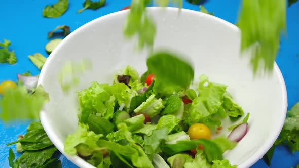 Fresh salad falling in bowl on blue background, top view