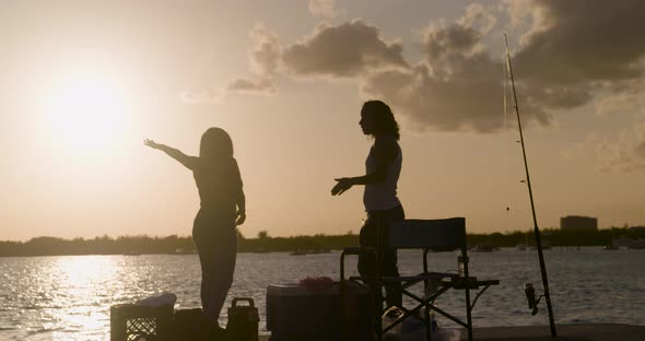 4K Silhouettes of Latinx women conversing on a fishing pier at sunset