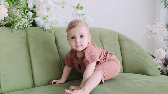 Little boy in a beige suit sits on a green sofa surrounded by beautiful flowers. Happy loving family