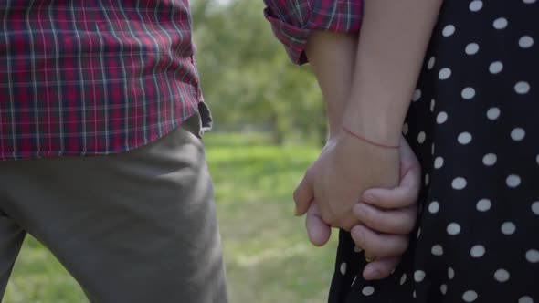 Close-up of Young Positive Couple Walking Through the Garden Holding Hands