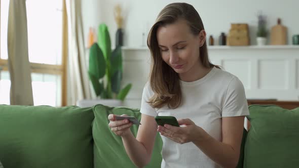 Young Woman Shopping Online with Credit Card and Smartphone While Sitting on Sofa at Home