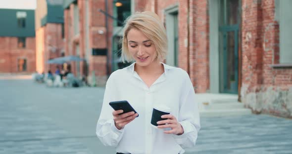 Businesswoman in White Shirt Surfing Internet on Smartphone while Walking at Street Outdoors.