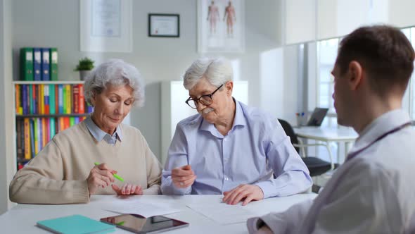 Senior Couple Sign Document in Doctor Office