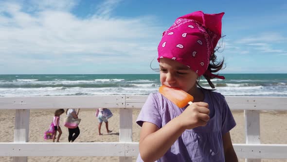 Baby Girl Child Biting Popsicle Ice Cream at Beach Bar Windy Sea Pink Bandana