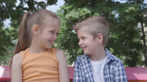 Portrait of Cute Blond Boy and Pretty Girl Sitting on the Swing on the Playground. Couple of Happy