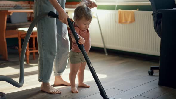 Mom and Baby Make Vacuum Cleaner Cleaning in Living Room As Mother and Child Play Game Indoors
