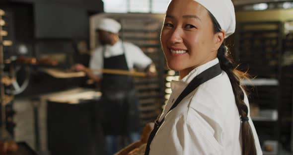 Animation of happy asian female baker holding basket with baguettes