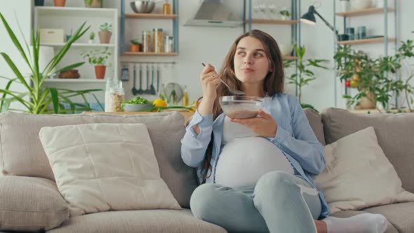 Beautiful Pregnant Woman Eating Healthy Breakfast Muesli With Nuts on the Couch