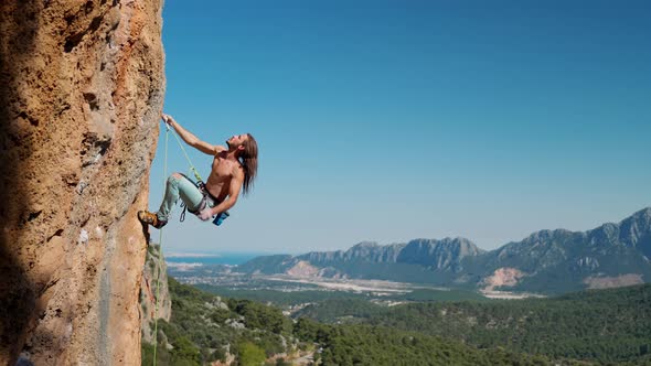 Slow Motion of Handsome Fit Body Man Rock Climber Hangs on Rope on Vertical Cliff Looks Up and Makes