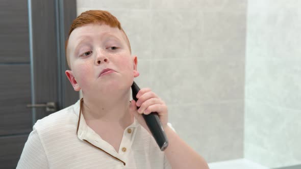 Little Boy is Shaving His Face with Electric Razor in the Bathroom