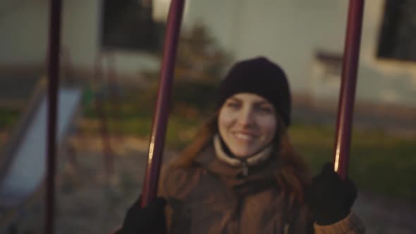 Young Attractive Redhaired Woman Swinging on a Swing in the City at Sunset or Sunrise