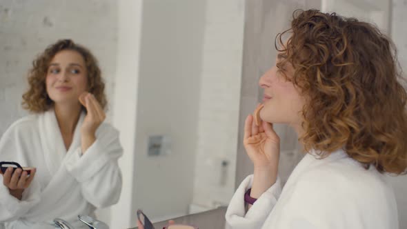 Beautiful Young Woman Applying Make-up Near Mirror in Bathroom