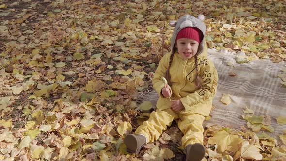 Small Cheerful Preschool Child Girl Warm Red Hat Eats Licks Large Candy on Stick