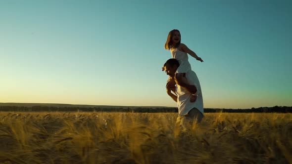 Happy father carrying little daughter on shoulders in wheat field