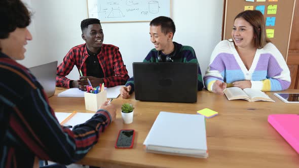 Young multiracial students reading books and using laptop in classroom while studying together