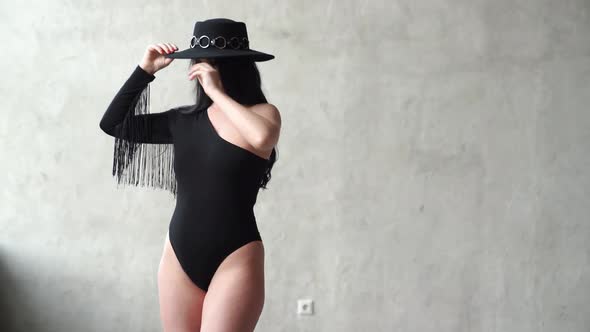Sexy Woman in a Black Bodysuit and Hat at the Gray Wall