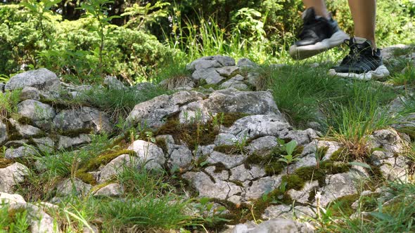 A woman walks down a rocky road in sneakers. Hiking in the mountains.