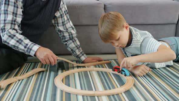 Joyful Kid Playing Toy Cars with Caring Grandfather Relaxing on Floor in Apartment alt