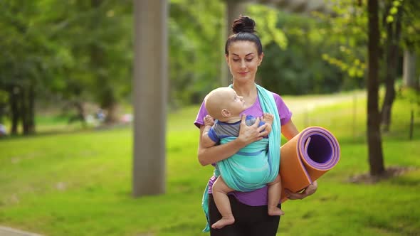 Mother Carrying Baby in Sling and Yoga Mat