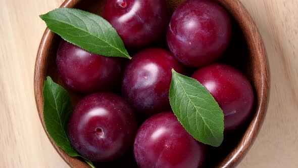 Plums rotating in wooden bowl top view