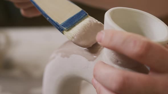 Close up view of female potter using glaze brush to paint on pot at pottery studio