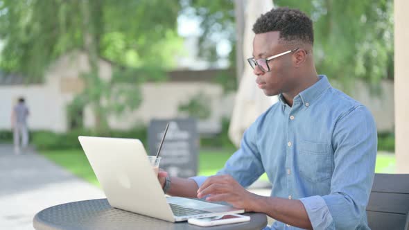 African Man with Coffee Working on Laptop in Outdoor Cafe