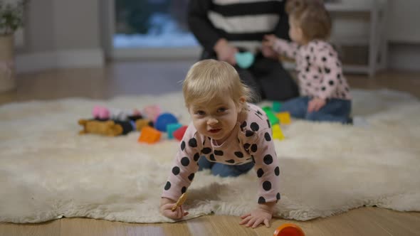 Portrait of Cute Baby Girl Looking at Camera with Twin Sister and Unrecognizable Mother at