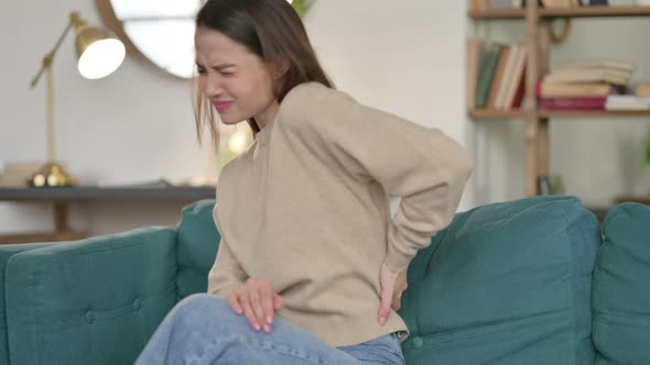 Young Woman with Back Pain Sitting on Sofa 