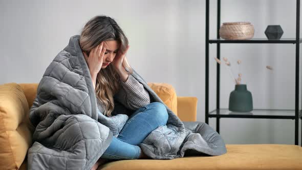 Upset Woman Sitting on Yellow Couch in Wrapped Plaid Having Headache Migraine