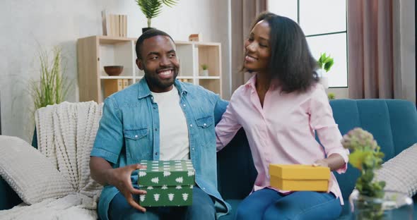 Couple Presenting Gift Boxes Into Camera when Sitting together on the sofa with huggs