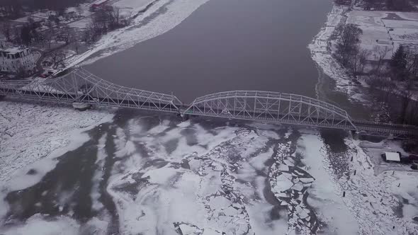 Drone flying high above swing bridge with big ice chunks in a snowy river during a winter storm.