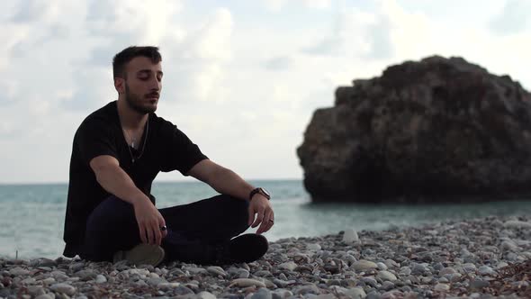 Handsome Man Meditating on the Background of a Rock and the Sea