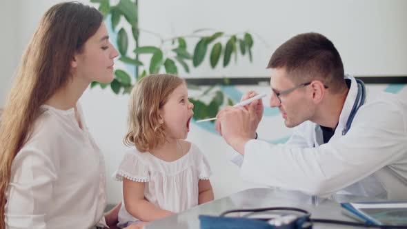 Male Doctor Pediatrician Examining an Ill Sad Kid at Medical Visit With Mother in the Hospital