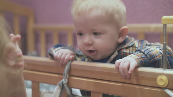 Little Baby Leans on Cot Playing with Elder Sister in Room