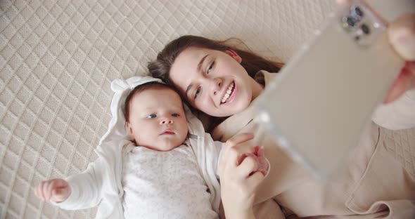 Mom Lies On The Bed With The Baby And Takes A Selfie On The Phone