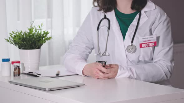 Unrecognizable Female Doctor in White Coat Sitting in Medical Office Room Table