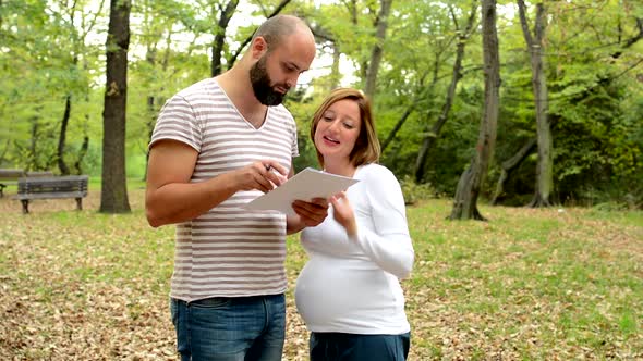 Handsome Man and Young Pregnant Woman Talk Together and Read Some Document in Park