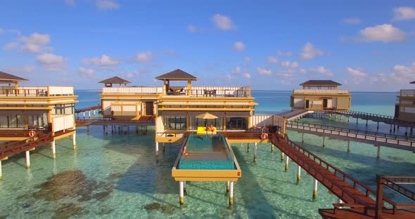 Aerial view of couple lounging by swimming pool on overwater bungalow, tropical island resort hotel.