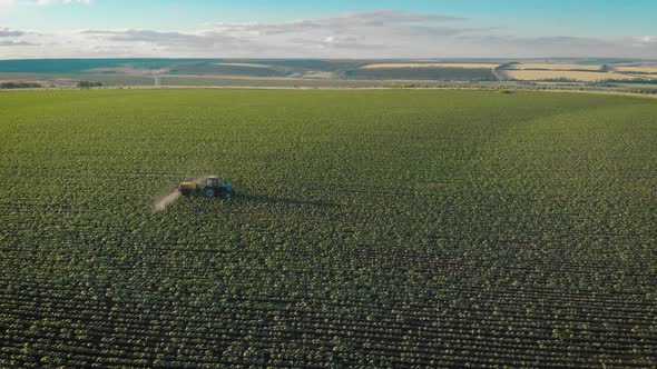 Aerial View of Farming Tractor Spraying on Field with Sprayer, Herbicides and Pesticides at Sunset